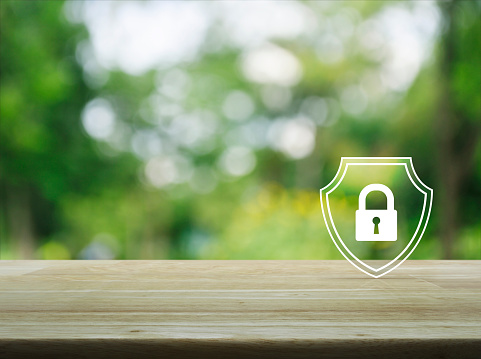Padlock with shield flat icon on wooden table over blur green tree in park, Business security insurance concept