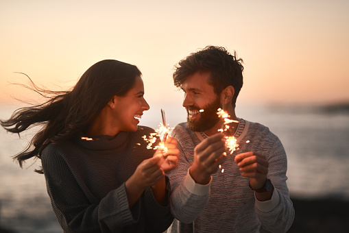 Shot of a happy young couple having fun with sparklers on the beach at sunset