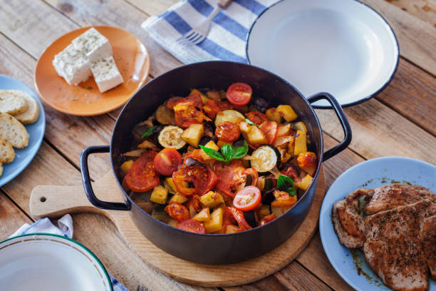 Briam, Greek ratatouille, roasted vegetables in cooking pan, with pork chops and feta cheese Briam, Greek ratatouille - baked zucchini and potatoes with eggplant, onion, tomato, cherry tomato, oregano and olive oil, with grilled pork chops and feta cheese, close-up ratatouille stock pictures, royalty-free photos & images