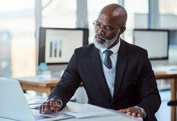 He's always a busy man Shot of a mature businessman working on a laptop in an office mature businessman stock pictures, royalty-free photos & images