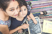 Indian Mother and Baby girl Writing and Drawing with chalk on the slate Board or black board