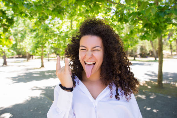 istock Joyful pretty young lady making horn gesture in park 1158344561