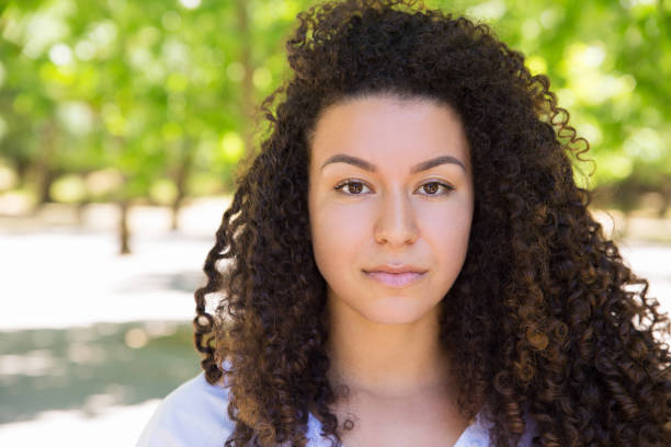 istock Serious pretty curly-haired lady posing at camera in park 1158344585