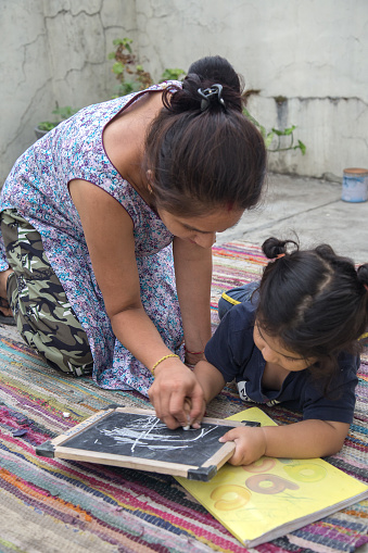 Indian Mother and Baby girl Writing and Drawing with chalk on the slate Board or black board