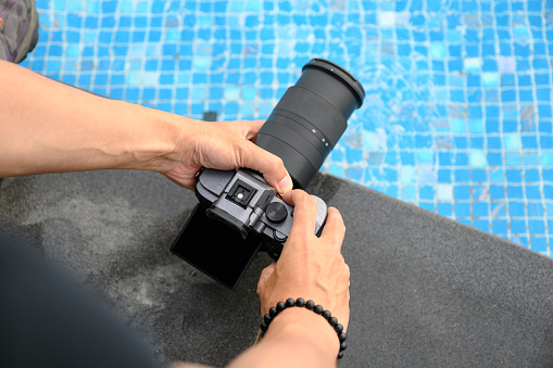 Hand holding mirrorless camera with zooming for take a photo on poolside