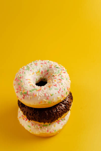 istock three white and black donuts on yellow background top view copy space 1158350347