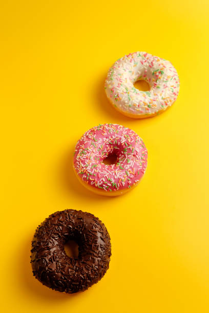istock pink white and black chocolate donuts on yellow background top view 1158354001