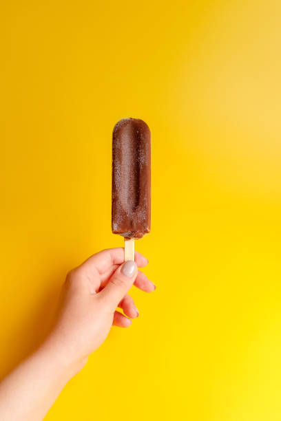 istock chocolate ice cream in hand on yellow background 1158355214