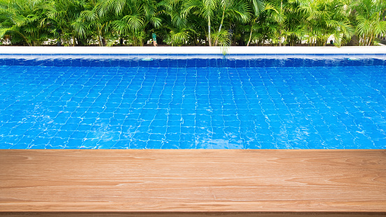 Empty wooden table beside resort swimming pool