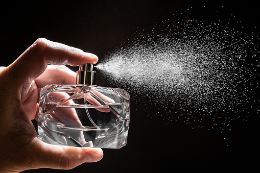 Unrecognizable woman sprays herself perfume on her wrist and is doing smelling gesture in front of white background.