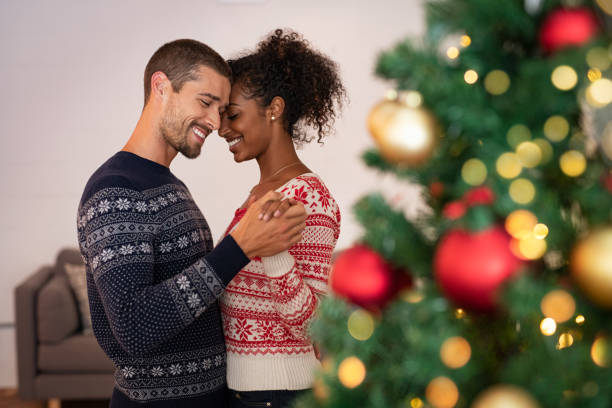 Multiethnic couple in love dancing during christmas Romantic multiethnic couple holding hands and dancing near christmas tree at home. Loving boyfriend and african girlfriend embracing with love at christmas holidays around lights. Young man and beautiful woman enjoying together new years eve. black man white woman couple stock pictures, royalty-free photos & images