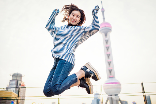 Young Asian woman jumping in front view of Oriental Pearl Tower.