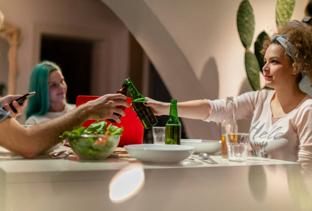 Cheers with her flatmate at the dinner table Young millennials flatmates in a toast with beer bottles at the dinner table flatmate stock pictures, royalty-free photos & images