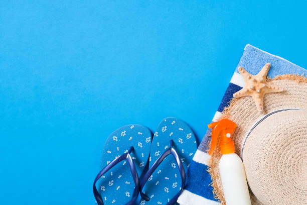 istock Summer beach flat lay accessories. Sunscreen bottle cream, straw hat, flip flops, towel and seashells on colored Background. Travel holiday concept with copy space 1158363855