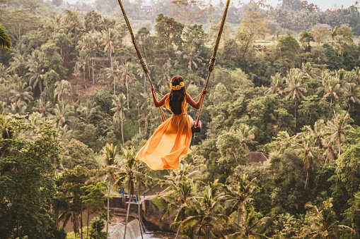 Photo of woman with long swing and forest view. Young woman swinging in the jungle rainforest of Bali island, Indonesia. Swing in the tropics. Women sit on swings at a height of more than twenty meters. In Indonesia Bali Province.