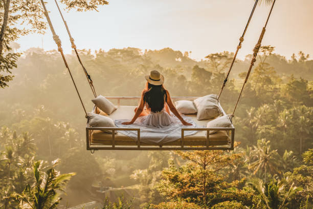 Enjoying the spectacular views Photo of a young woman sitting on the swing. Jungle Bed hanging over the tropical forest with Caucasian female resting while looking at the view, Bali, Indonesia. Rear view of a female sitting and enjoying the view. swinging stock pictures, royalty-free photos & images