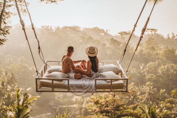 In you I've found a special kind of love Photo of the couple in love. The morning in a bed filled with tenderness and romance. happy man and a woman sitting on flying bed over the tropical Forrest. Bali, Indonesia. Successful couple relaxing at a luxury villa with a beautiful view at the rice terraces,  honeymoon at Bali, Ubud. bali stock pictures, royalty-free photos & images