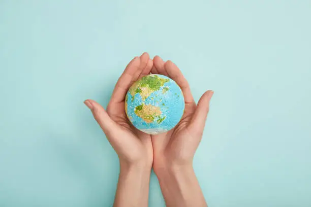 Photo of top view of woman holding planet model on turquoise background, earth day concept