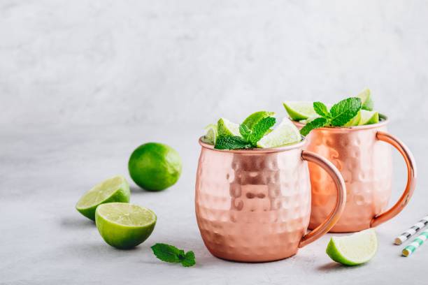 istock Moscow mule ice cold cocktail in copper cup with lime and and mint on gray stone background 1158381579