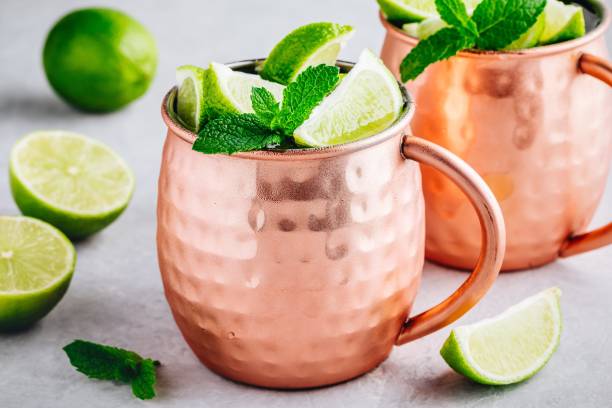 istock Moscow mule ice cold cocktail in copper cup with lime and and mint on gray stone background 1158381639