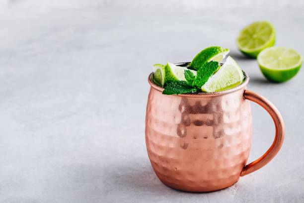 istock Moscow mule ice cold cocktail in copper cup with lime and and mint on gray stone background 1158381705