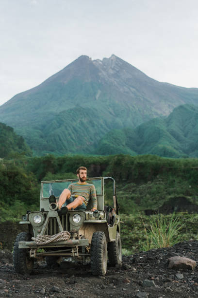 istock Man sitting on old fashioned SUV on the background of Merapi volcano 1158381714