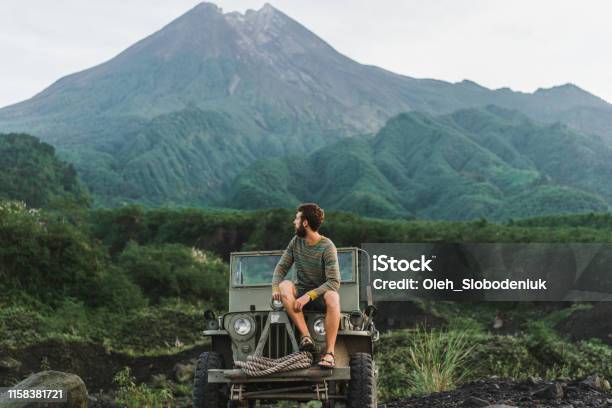 Man Sitting On Old Fashioned Suv On The Background Of Merapi Volcano Stock Photo - Download Image Now