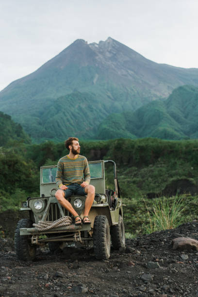 istock Man sitting on old fashioned SUV on the background of Merapi volcano 1158381722
