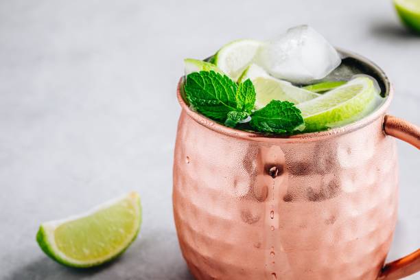 istock Moscow mule ice cold cocktail in copper cup with lime and and mint on gray stone background 1158381733