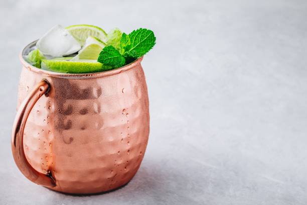 istock Moscow mule ice cold cocktail in copper cup with lime and and mint on gray stone background 1158381741