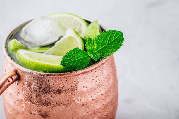 istock Moscow mule ice cold cocktail in copper cup with lime and and mint on gray stone background 1158381773