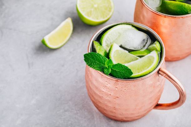 istock Moscow mule ice cold cocktail in copper cup with lime and and mint on gray stone background 1158381789
