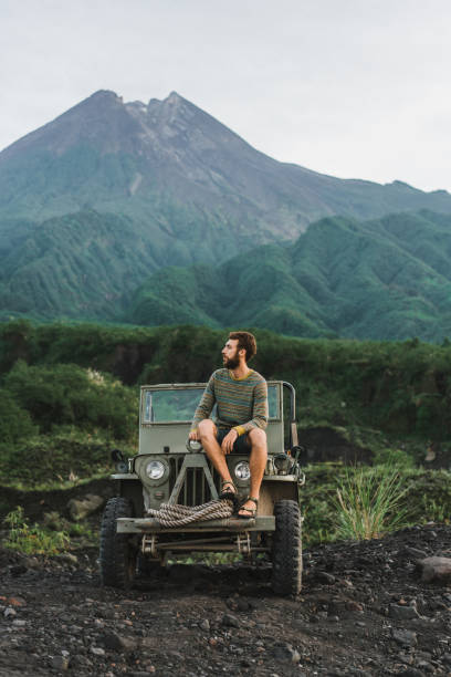 istock Man sitting on old fashioned SUV on the background of Merapi volcano 1158385591