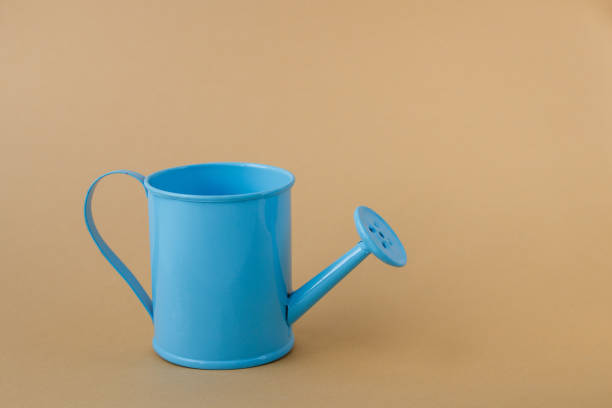 istock Toy blue watering can against a light brown background. 1158385842