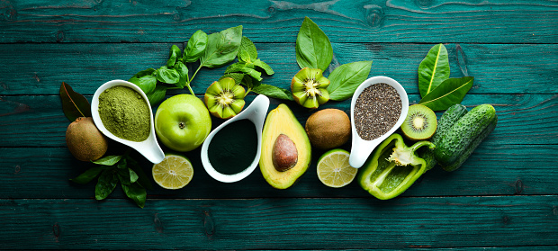 Healthy Green food. Fruits and vegetables - avocado, lime, onion, apple, kiwi, spirulina. On a blue wooden background. Top view. Free space for your text.
