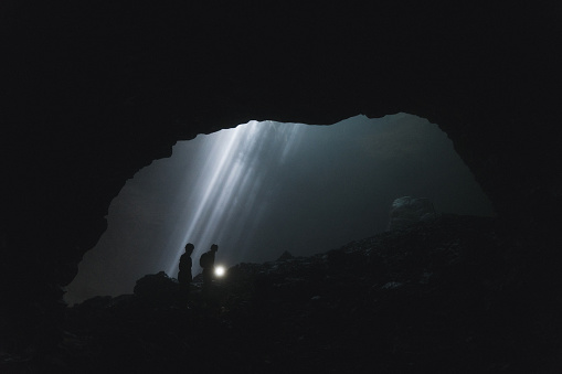 Silhouettes of two people walking  in Jomblan Cave  on the background of sunbeams, Java, Indonesia
