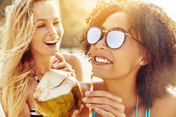 istock Laughing female friends sipping from coconuts on a sandy beach 1158395872