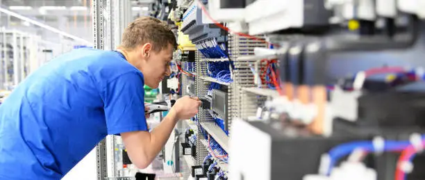 young apprentice worker in an industrial company assembling electronic components in the mechanical engineering of a modern factory