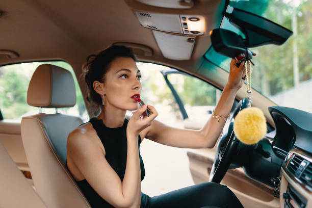 istock Young elegant woman looking in the car view mirror while applying makeup, lipstick on the lips 1158399336