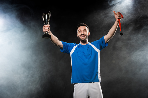handsome champion holding trophy and medals in hands on black with smoke