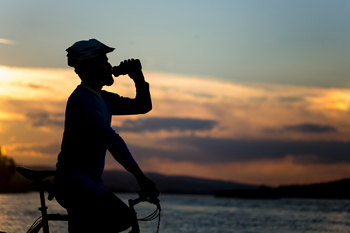 Silhouette of a cyclist drinking from a water bottle.