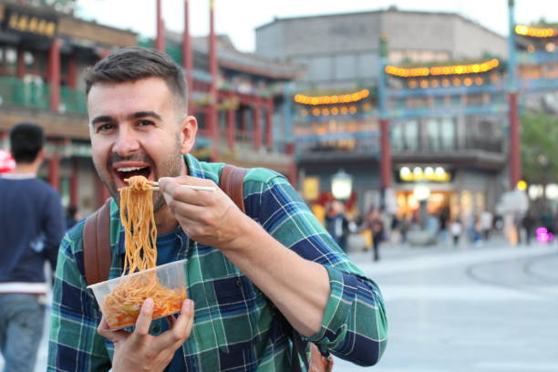 istock Cute guy eating Asian noodles outdoors 1158407549