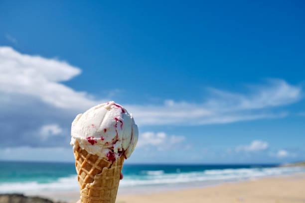 istock Hand holding a raspberry ripple ice cream overlooking Fistral Beach, Cornwall on a sunny June day. 1158408964