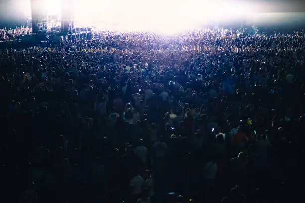 Photo of The bright light of the stage illuminates a huge concert crowd.