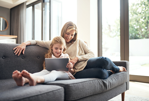 Full length shot of an attractive mature woman and granddaughter using a digital tablet while sitting on the sofa at home