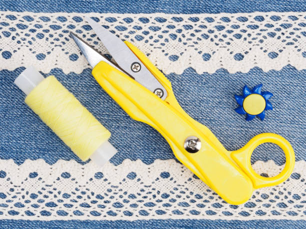 istock White lace, yellow thread and scissors, blue button on jeans background. Stitching still life 1158418296
