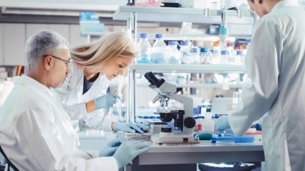 grupa naukowców w white coats pracuje z mikroskopem w nowoczesnym laboratorium high-tech. genetyka i badania farmaceutyczne. - scientist research test tube lab coat zdjęcia i obrazy z banku zdjęć