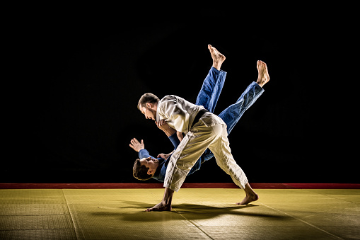 Judo practitioner throwing his sparring partner on to a tatami mat during a duel in a dojo.