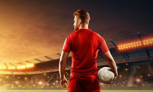 istock Soccer player in uniform with a ball on a floodlit stadium. Back view 1158422355
