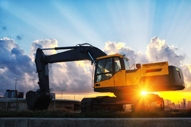 istock Mechanical digger on a construction site, backlit by a beautiful sunset over a city 1158423175
